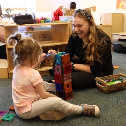 Teacher sitting with child on floor with toy