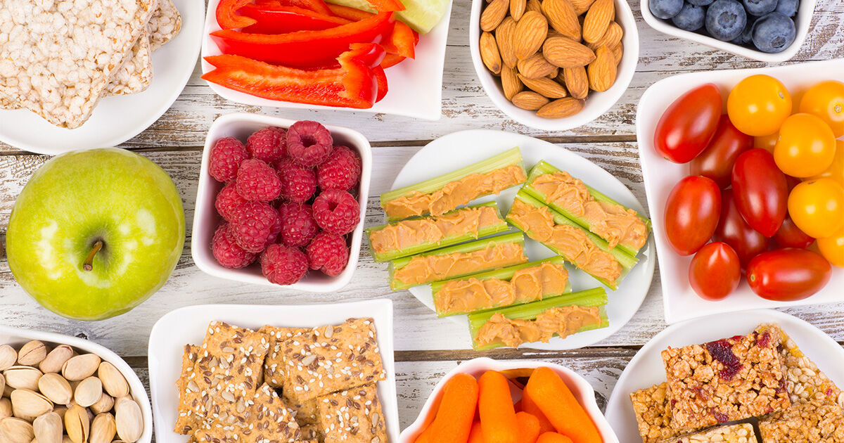 Healthy Snacks-Header-4 Assortment of healthy snacks including fresh fruits, vegetables, nuts, crackers, and celery topped with peanut butter.
